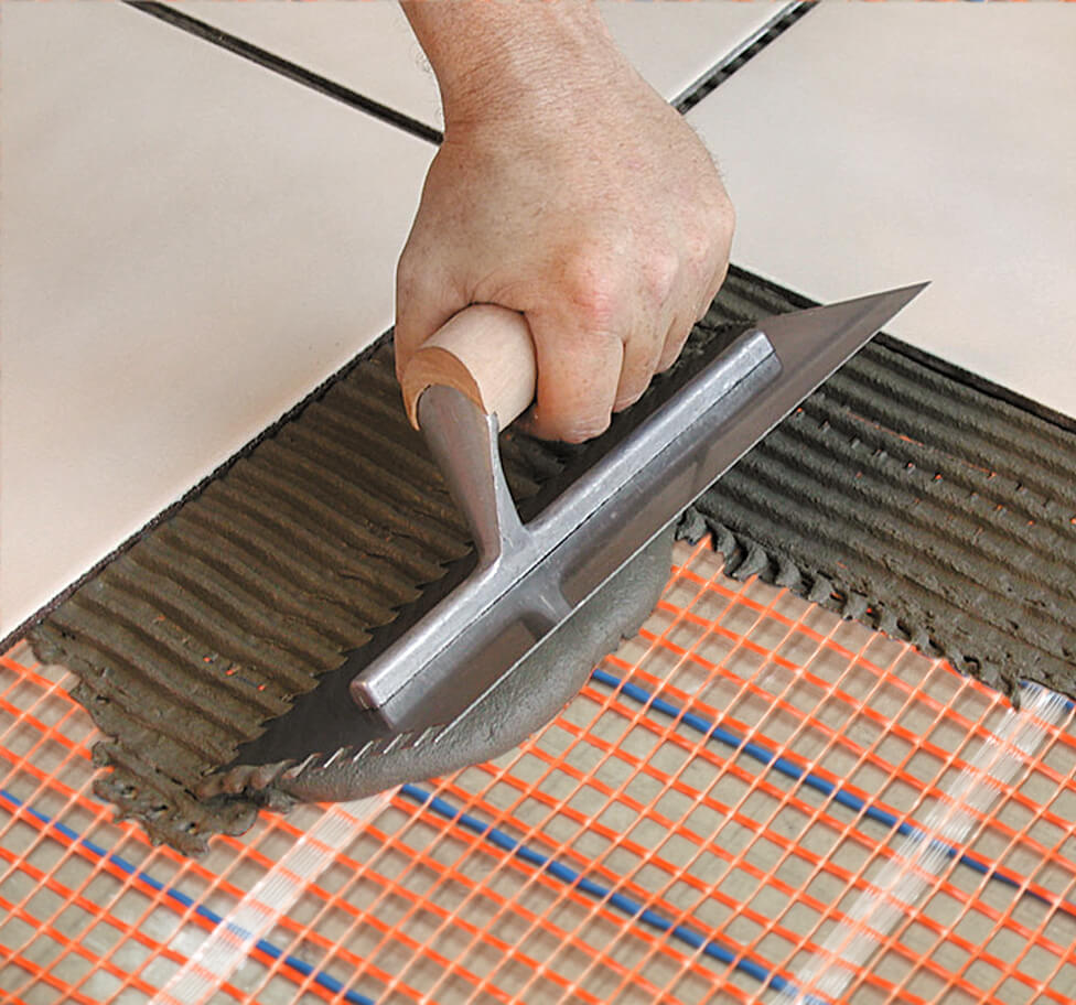 A contractor applying Thinset over a radiant floor heating mat.